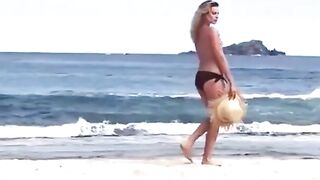 Margot Robbie topless while in panties walking on a beach.